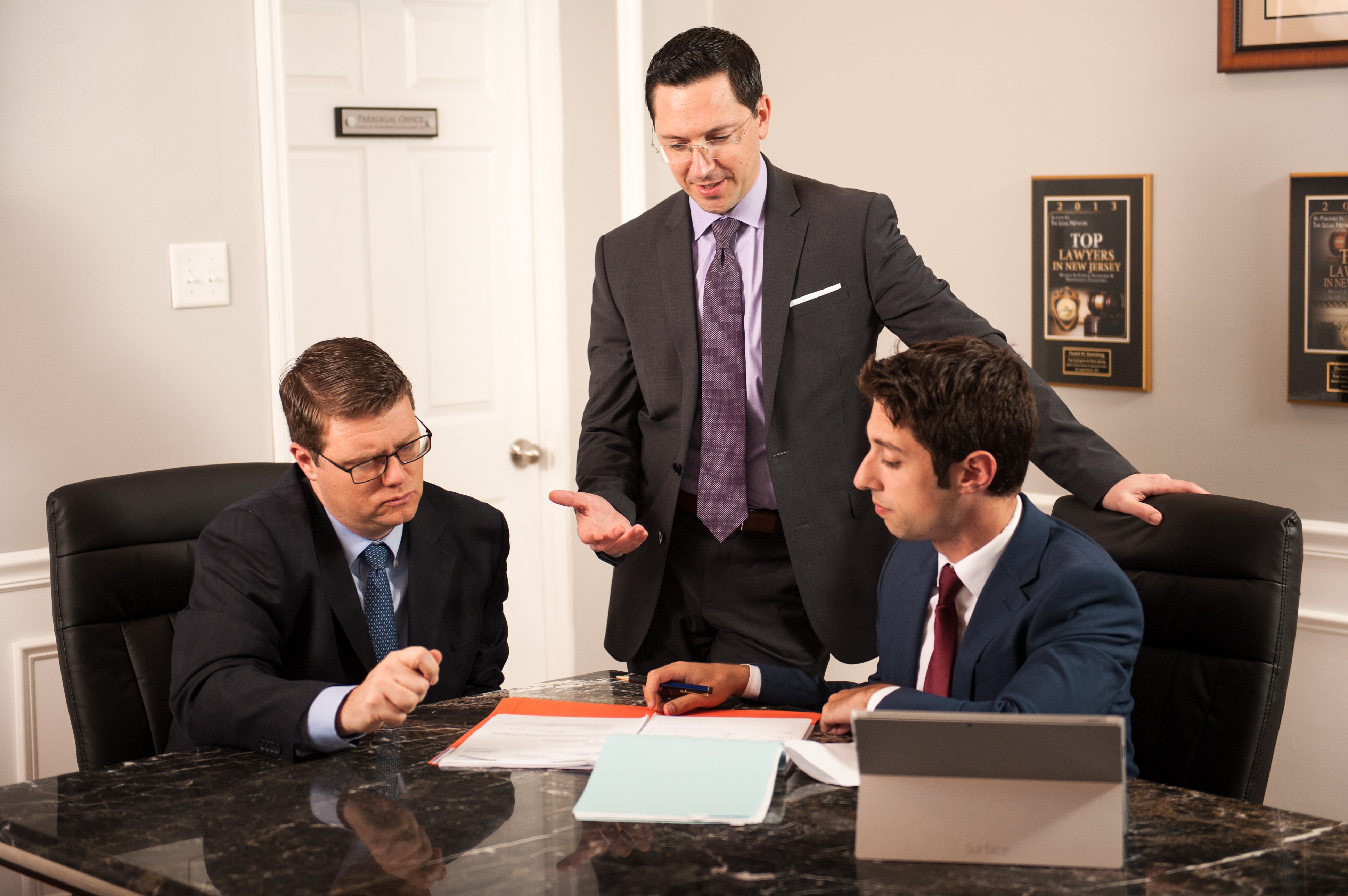 Attorneys Daniel M. Rosenberg, Robert M. Perry, and Nathan J. Mammarella of Rosenberg | Perry & Associates discussing case files around a marble table in their office