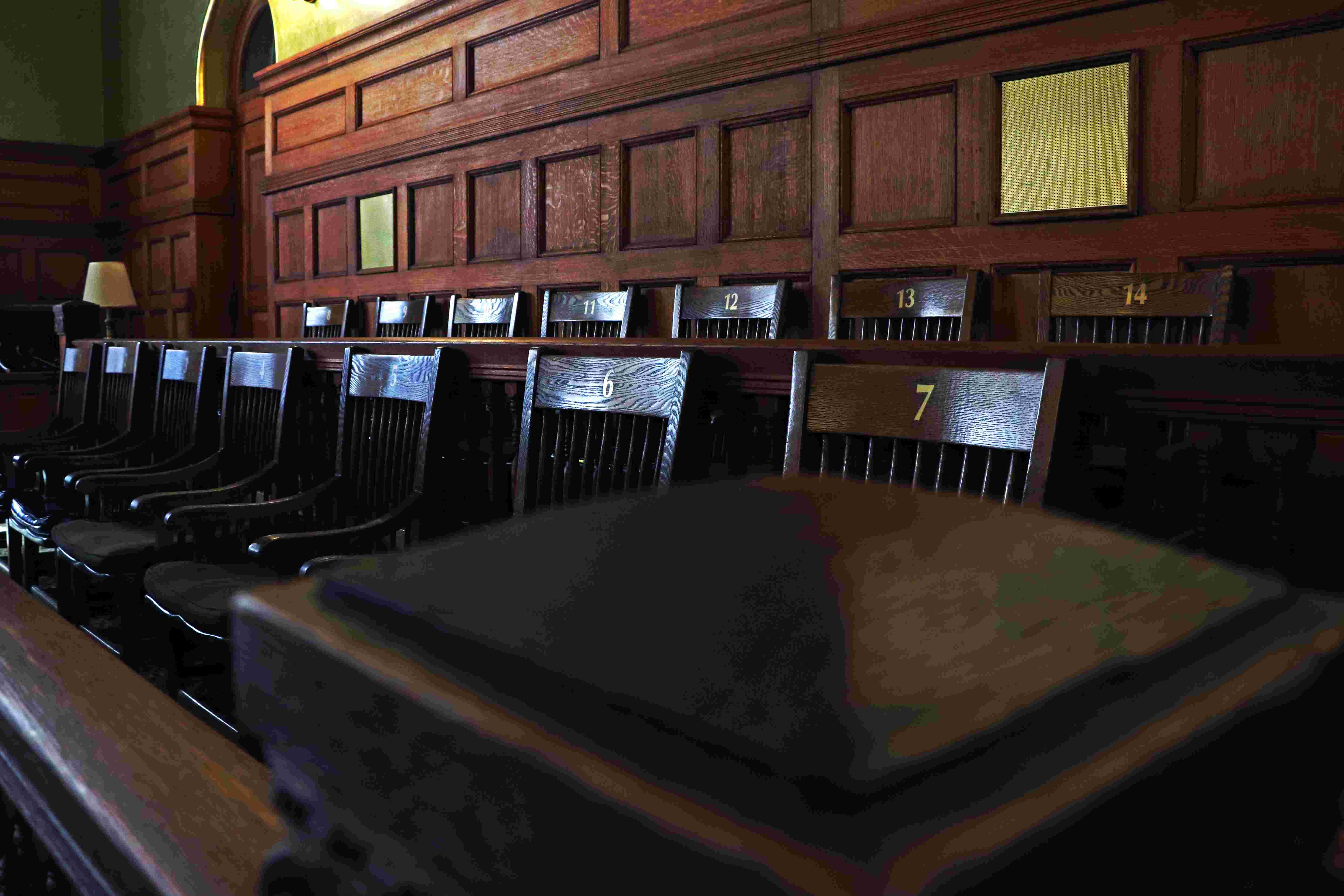 Empty wooden chairs numbered in two rows inside a historic, wood-paneled courtroom jury box