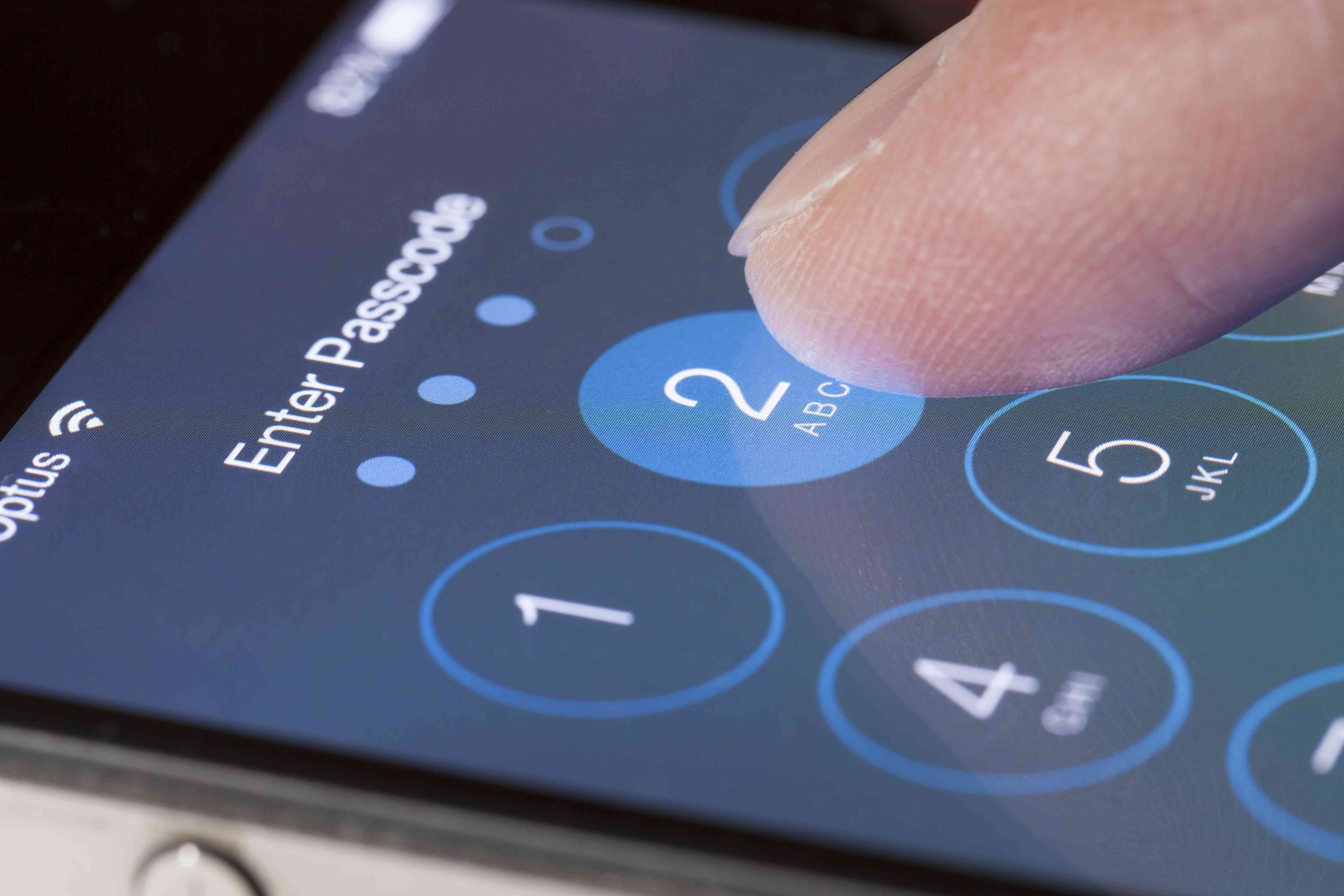 A finger pressing the number 2 on an Apple iPhone passcode screen.