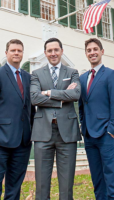 Attorneys Daniel M. Rosenberg, Robert M. Perry, and Nathan J. Mammarella of Rosenberg | Perry & Associates standing in front of the firm's white building