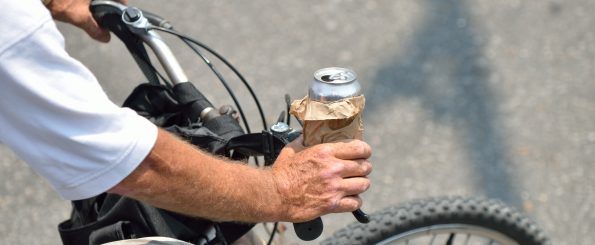 Close-up of a person riding a bicycle while holding an open aluminum can wrapped in a brown paper bag