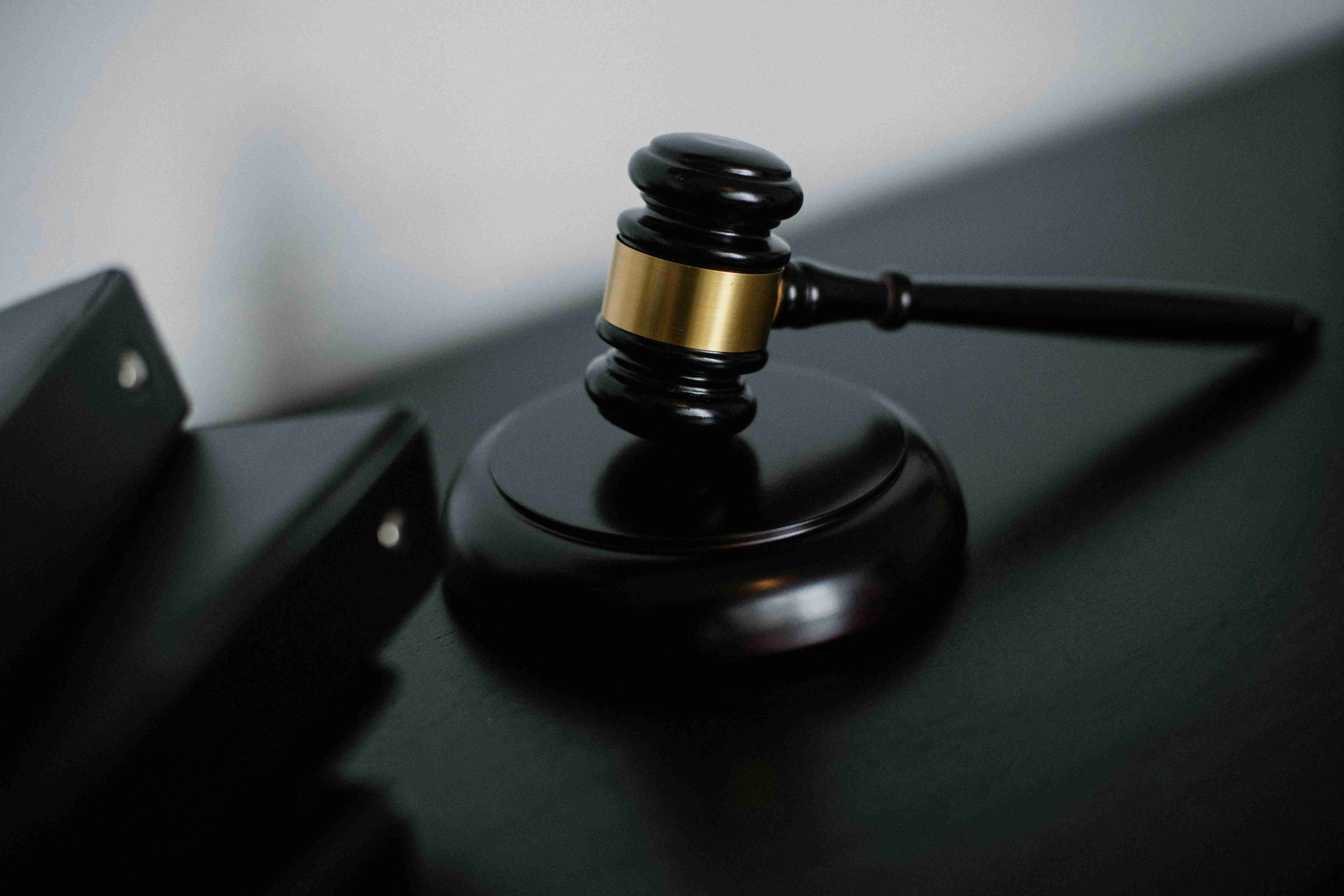 A dark wooden judge's gavel and sound block resting on a desk next to several black legal binders